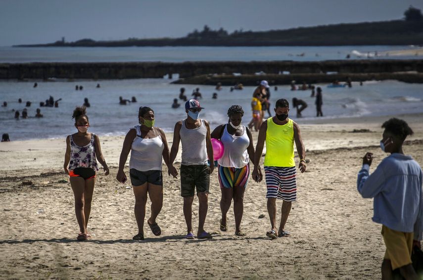 Personas que usan máscaras como precaución contra la propagación del nuevo coronavirus caminan en la playa en La Habana, Cuba, el domingo 11 de octubre de 2020.