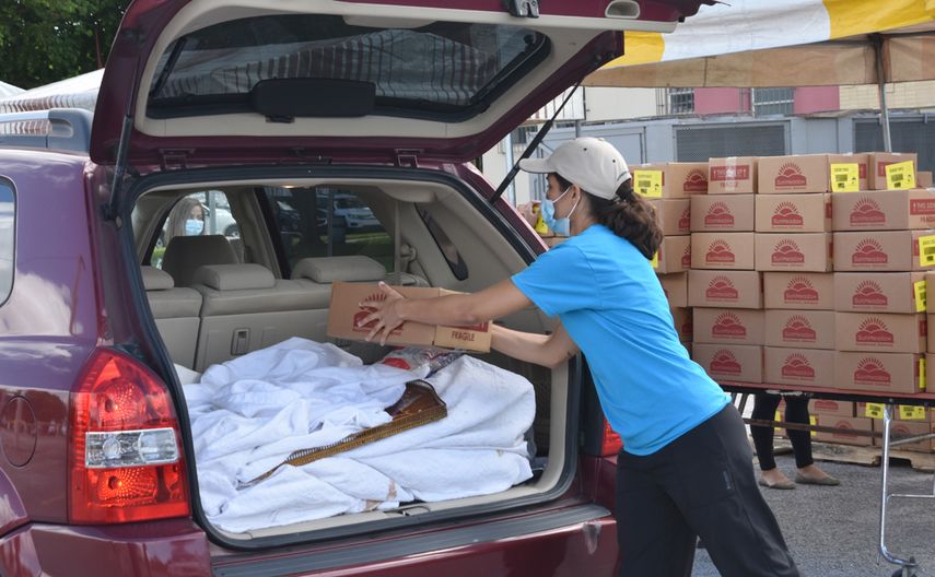 Una voluntaria deposita alimentos a un necesitado en el maletero del autom&oacute;vil.