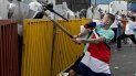 Un manifestante envuelto en una bandera costarricense y con un tubo de metal se enfrenta a la policía antidisturbios durante una protesta contra la moción del gobierno de aumentar los impuestos para llegar a un acuerdo crediticio con el Fondo Monetario Internacional (FMI), frente a la casa presidencial en San José. el 12 de octubre de 2020. Un manifestante envuelto en una bandera costarricense y con un tubo de metal se enfrenta a la policía antidisturbios durante una protesta contra la moción del gobierno de aumentar los impuestos para llegar a un acuerdo crediticio con el Fondo Monetario Internacional (FMI), frente a la casa presidencial en San José. el 12 de octubre de 2020.