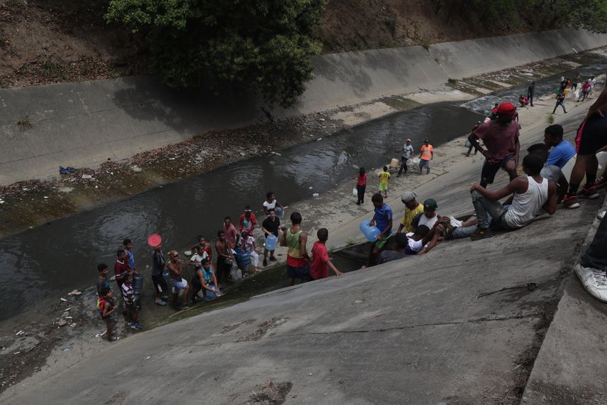 Personas recogen agua este lunes en el río Guaire, que va paralelo a la autopista Francisco Fajardo, en Caracas.&nbsp;