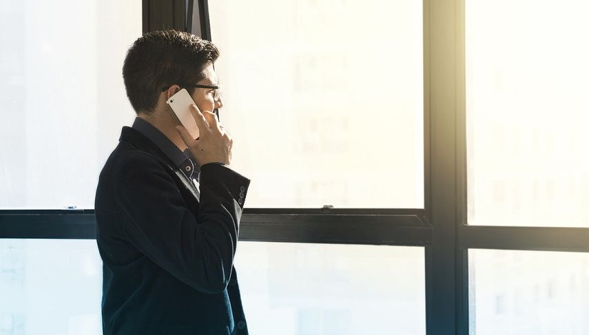 Un hombre mira por una ventana mientras conversa por un tel&eacute;fono celular.