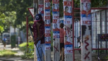 Un hombre barre una acera frente a postes con propaganda política en una calle de Managua el 3 de noviembre de 2017, durante el inicio del silencio electoral previo a los comicios.