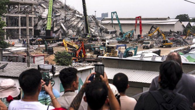 Personas toman una fotografía mientras se utiliza maquinaria para retirar los escombros en el lugar del derrumbe de un edificio en construcción en Bangkok el 31 de marzo de 2025, tres días después de que un terremoto azotara el centro de Myanmar y Tailandia.&nbsp;