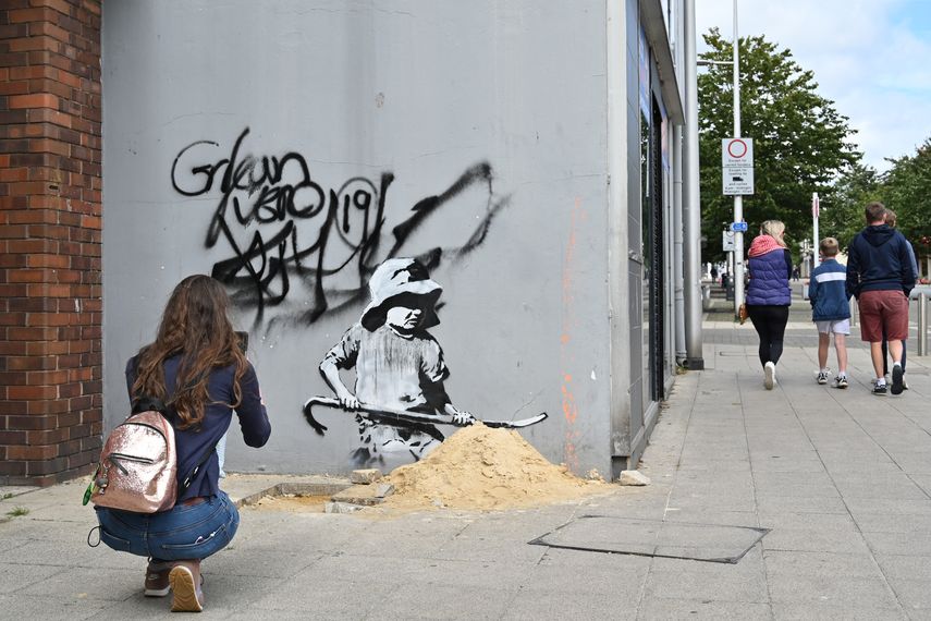 Una mujer toma una fotografía de un estarcido de un niño cavando en la arena con el sello distintivo del artista callejero Banksy en una pared en Lowestoft en la costa este de Inglaterra el 8 de agosto de 2021.