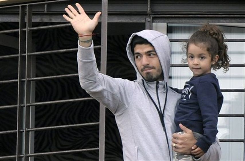El uruguayo Luis Suárez carga a su hija y saluda a los seguidores que acudieron a manifestarle apoyo, desde el balcón de su casa en las afueras de Montevideo, el viernes 27 de junio de 2014 (AP Foto/Matilde Campodonico)