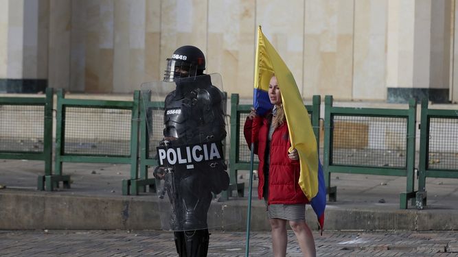 En esta imagen, tomada el 21 de septiembre de 2020, una mujer con una bandera colombiana, junto a un agente antimotines durante una protesta en Bogot&aacute;, Colombia. Sindicatos y grupos de estudiantes convocaron manifestaciones contra la brutalidad policial, la inseguridad y la crisis provocada por la pandemia del coronavirus.&nbsp;