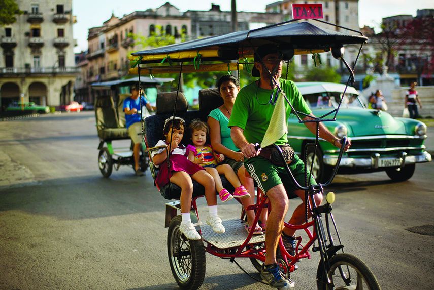 Un conductor de bicitaxis traslada una familia cubana por las calles de La Habana. (AP)