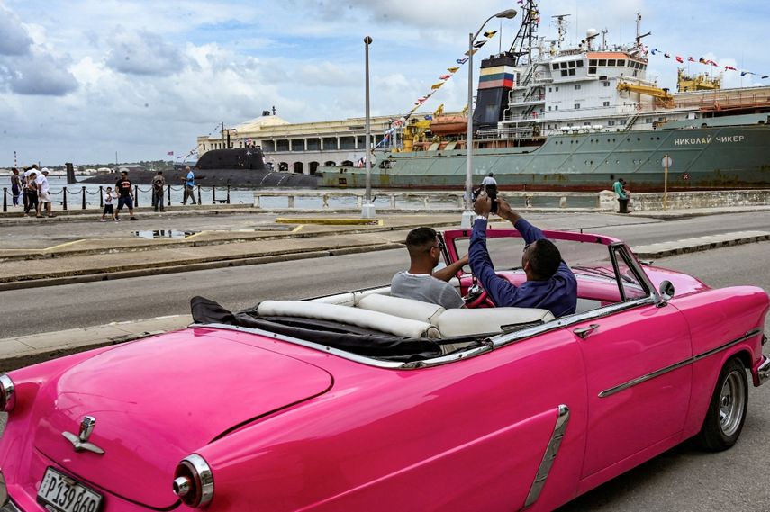 Un hombre toma fotografías del submarino de propulsión nuclear Kazán (izq.) y del remolcador de rescate y salvamento Nikolai Chiker (der.), parte del destacamento naval ruso que visita Cuba, después de su llegada al puerto de La Habana el 12 de junio de 2024.