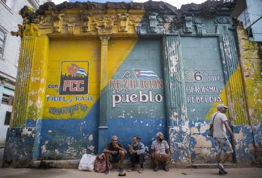 Varias personas sentadas en la acera de una calle en Cuba.&nbsp;