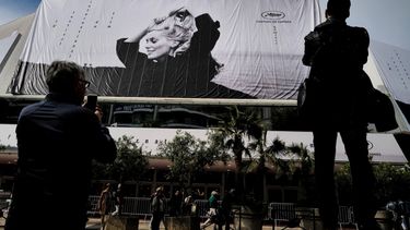 La gente observa cómo los trabajadores cuelgan el cartel oficial del 76º Festival de Cine de Cannes con una fotografía de la actriz Catherine Deneuve de Jack Garofalo, en la fachada del Palais des Festivals en Cannes, sureste de Francia, el 14 de mayo de 2023.