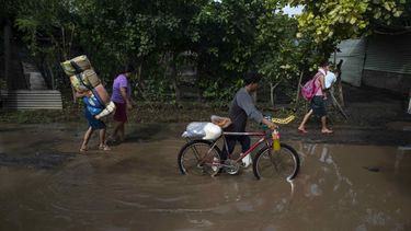 Varias personas caminan con frazadas y provisión por una calle inundada después que un cauce se desbordara.