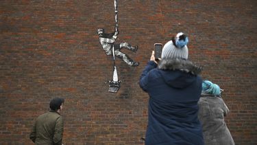 En esta foto de archivo tomada el 2 de marzo de 2021, el público hace una pausa para mirar una obra de arte del artista callejero Banksy en el costado de la prisión de Reading en Reading, al oeste de Londres.&nbsp;