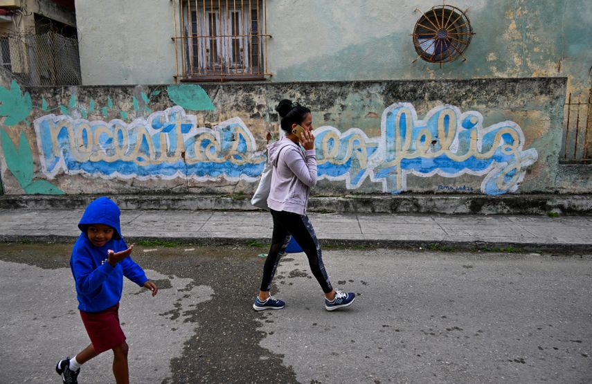 Los cubanos pasan junto a un graffiti que dice Necesitas ser feliz del artista cubano Mr. Sad en La Habana, el 12 de diciembre de 2024.