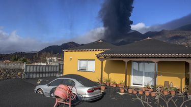 Una capa de ceniza volcánica cubre una casa, un automóvil y sus alrededores mientras en el fondo un volcán sigue en erupción en la isla canaria de La Palma, España, el lunes 4 de octubre de 2021. 