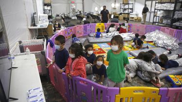 Niñas y niños migrantes de 3 a 9 años que viajaban sin un adulto ven televisión desde un corral de juego el martes 30 de marzo de 2021 en una instalación de la Oficina de Aduanas y Protección Fronteriza, en el Rio Grande Valley en Donna, Texas.