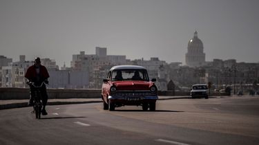 Un automóvil y una bicicleta clásicos estadounidenses comparten el camino en el Malecón en La Habana, Cuba.