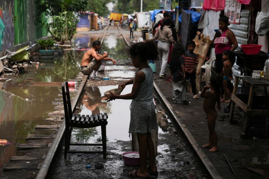 Una niña migrante lava un plato después de un aguacero en un campamento instalado a lo largo de las vías del tren Vallejo, el jueves 18 de julio de 2024, en Ciudad de México.