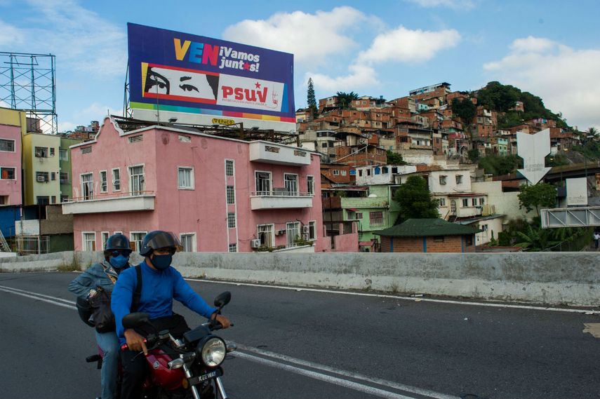 La gente pasa en bicicleta frente a una valla publicitaria con propaganda política que representa los ojos del fallecido presidente venezolano Hugo Chávez, en Caracas el 2 de diciembre de 2020 antes de las elecciones parlamentarias en el país. Venezolano celebrará elecciones legislativas el 6 de diciembre.