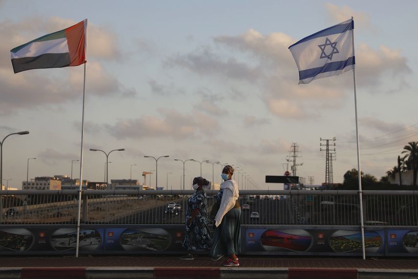 Mujeres con cubrebocas para evitar la propagaci&oacute;n del coronavirus pasan entre las banderas de los Emiratos &Aacute;rabes Unidos e Israel en el Puente de la Paz en Netanya, Israel, el domingo 16 de agosto de 2020. (AP Foto/Ariel Schalit)