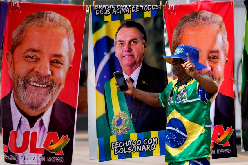 Un manifestante vestido con los colores de la bandera brasileña se presenta frente a las toallas de un vendedor ambulante a la venta con los candidatos presidenciales brasileños, el actual presidente Jair Bolsonaro, al centro, y el expresidente Luiz Inácio Lula da Silva, en Brasilia,