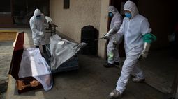 Trabajadores con equipos de protección colocan el cuerpo de una víctima de COVID-19 en un ataúd el martes 23 de junio de 2020, en la Ciudad de México. 