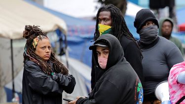 Manifestantes observan mientras la polic&iacute;a de Seattle termina de investigar un auto involucrado en un tiroteo el lunes 29 de junio de 2020 en Seattle, en donde las calles est&aacute;n bloqueadas en lo que se ha nombrado la zona de protesta occupied del Capitolio.&nbsp;