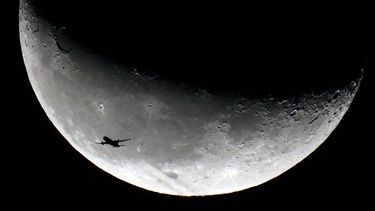Se recorta la silueta de un avión contra la luna creciente menguante sobre la ciudad de Kuwait a primera hora del 6 de enero de 2024.