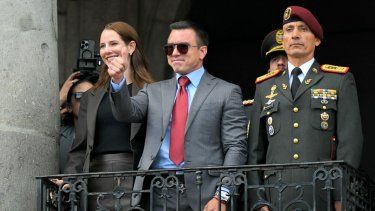 El presidente reelegido de Ecuador, Daniel Noboa, saluda a sus simpatizantes, acompañado por su esposa, Lavinia Valbonesi (izq.), y el jefe de la Casa Militar Presidencial, Milton Rodríguez, desde un balcón del Palacio Presidencial de Carondelet durante la ceremonia de cambio de guardia en Quito el 15 de abril de 2025.&nbsp;