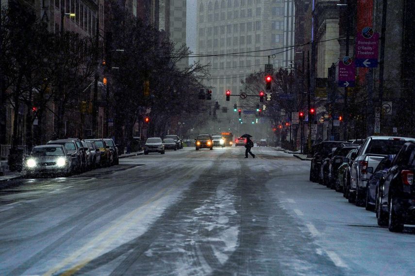 Un peatón utiliza un paraguas mientras cruza la Avenida Liberty en el centro de Pittsburgh, mientras comienza a nevar en medio de una tormenta, el domingo 16 de enero de 2022.