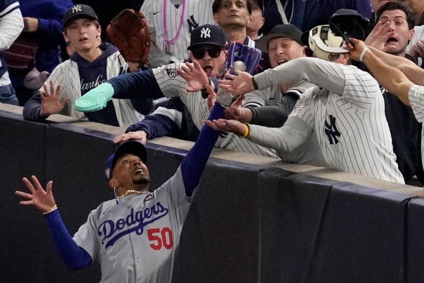 Fanáticos interfieren en un elevado de foul atrapado por el jardinero derecho Mookie Betts, de los Dodgers de Los Ángeles, durante el primer inning del cuarto juego de la Serie Mundial, el martes 29 de octubre de 2024, en Nueva York.