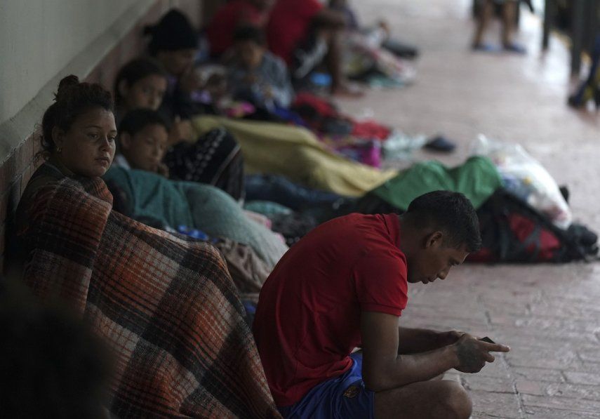 Migrantes venezolanos sentados junto a la pared de un edificio mientras se resguardan de la lluvia, el sábado 13 de mayo de 2023.&nbsp;
