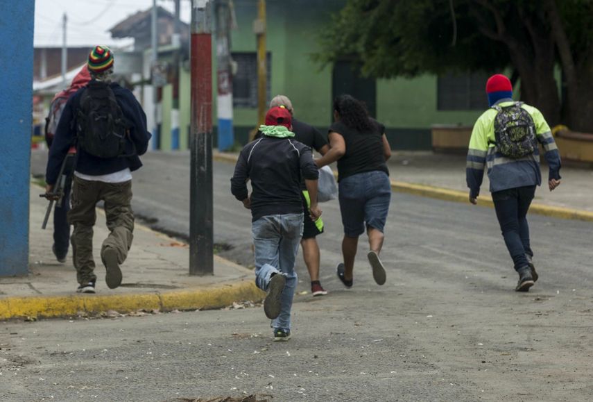 Dos mujeres corren junto a varios jóvenes que portan lanza morteros durante un enfrentamiento con la Policía Nacional.&nbsp;