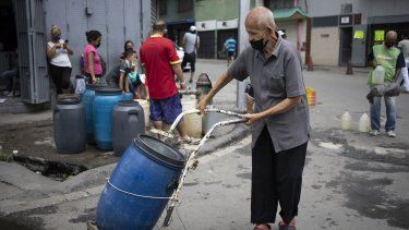 Un hombre, protegido con una mascarilla, empuja un recipiente que llenó de agua en un grifo callejero, en Caracas, Venezuela, el 20 de junio de 2020.&nbsp;