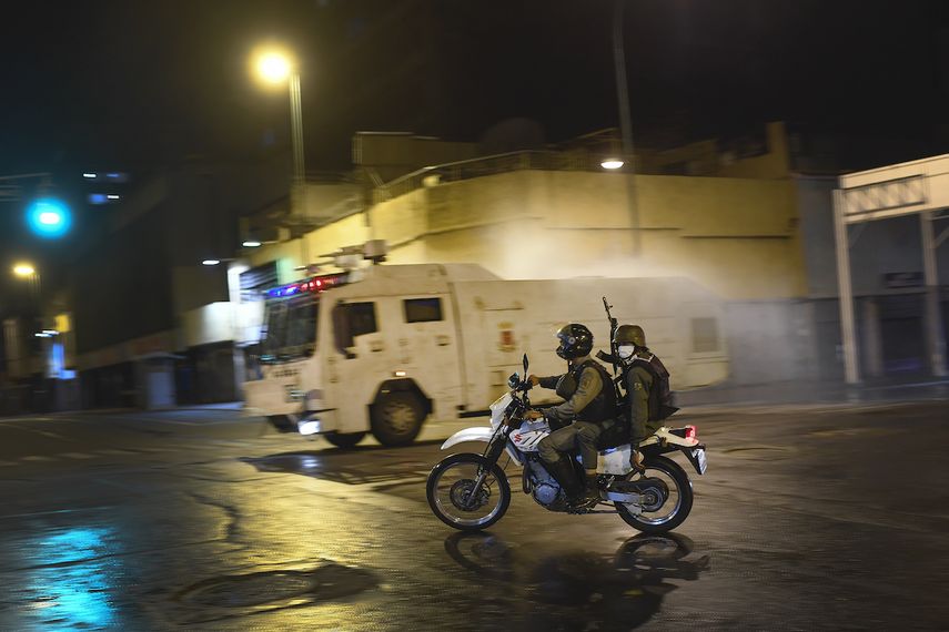 Miembros de la Guardia Nacional Bolivariana viajan en motocicleta mientras una tanqueta arroja desinfectante en las calles de Caracas, Venezuela, el s&aacute;bado 21 de marzo de 2020.&nbsp;