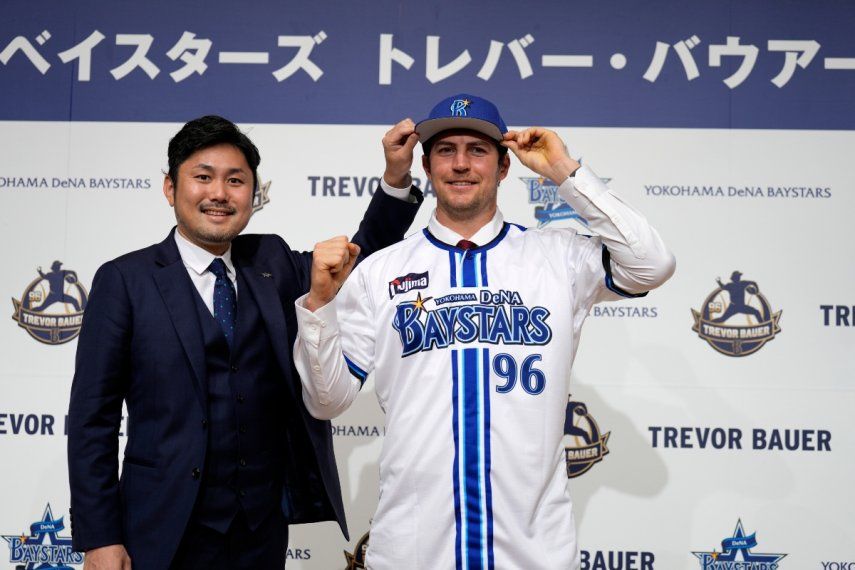 Trevor Bauer porta el uniforme y gorra del Yokohama DeNA BayStars junto al director de operaciones del equipo, Tatsuhiro Hagiwara, en la conferencia de prensa de su presentación, el viernes 24 de marzo del 2023.