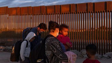 Una familia de migrantes camina se traslada cerca del muro fronterizo entre Estados Unidos y México.