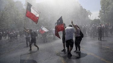 Manifestantes con banderas de Chile reciben chorros de agua lanzados por la polic&iacute;a en el centro de Santiago en una nueva jornada de protestas sociales en la naci&oacute;n sudamericana, el mi&eacute;rcoles 23 de octubre de 2019.&nbsp;