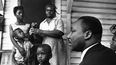 El Dr. Martin Luther King Jr., a la derecha, conversa con afroamericanos de Greenwood, Mississippi, en el porche de su casa el 21 de julio de 1964, durante su campaña puerta a puerta, diciéndoles que se registren para votar y apoyen a su partido Demócrata por la Libertad de Mississippi.