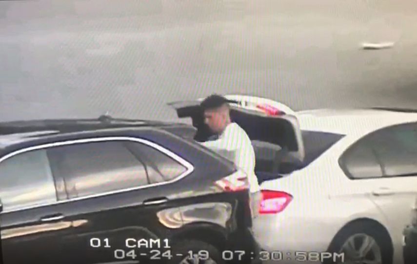 Uno d elos tres ladrones aborda el maletero de un auto estacionado.