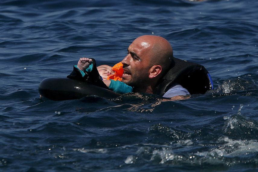 Un refugiado sirio que sostiene a un bebé en un flotador nada hacia la costa luego de que su bote se desinfló cerca de la isla griega de Lesbos. (REUTERS)