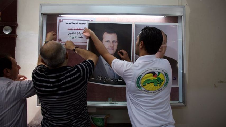 Autoridades electorales colocan un cartel con la imagen del presidente sirio Bashar Assad en una casilla de votación en Damasco, Siria (AP)