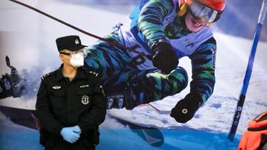 Un agente de policía con mascarilla y gafas protectoras contra el COVID-19, de pie ante un cartel con la imagen de una esquiadora con motivo a los Juegos Olímpico de Invierno, a los que Estados Unidos solo enviará a sus atletas