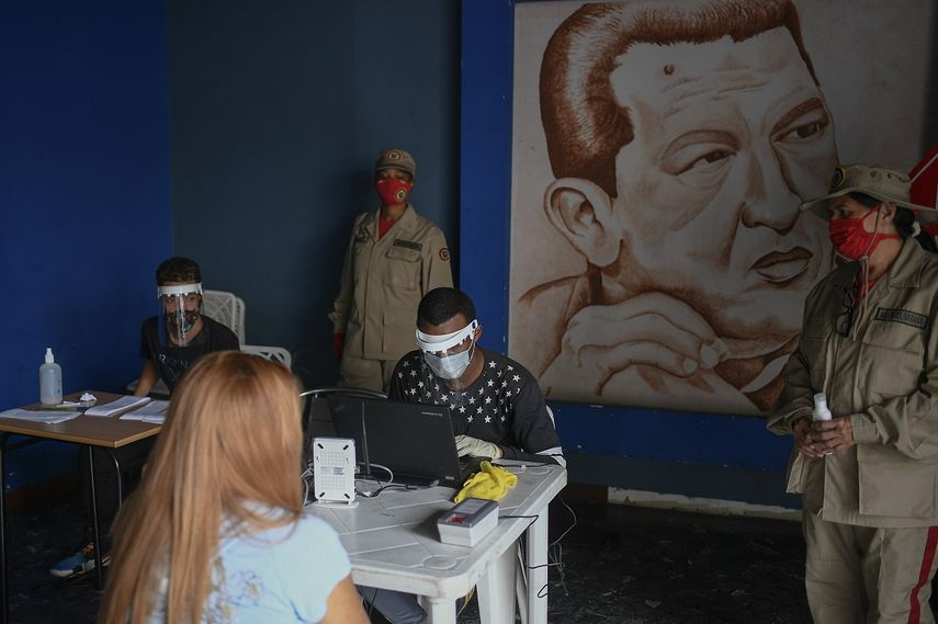Personal del Consejo Nacional Electoral (CNE) con equipo protector del coronavirus revisa archivos en Caracas, Venezuela, con miras a las elecciones legislativas del 6 de diciembre. Detrás suyo hay una imagen de Hugo Chávez. 