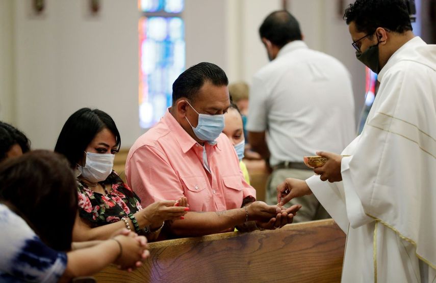 La pandemia del coronavirus obliga a cambios en los servicios religiosos. El padre Praveen Lakkisettit, derecha, utiliza una mascarilla mientras da la comuni&oacute;n a feligreses durante una misa en la iglesia cat&oacute;lica Cristo Rey en San Antonio, el martes 19 de mayo de 2020.&nbsp;