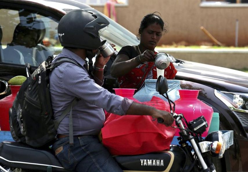  Un motorista hace una parada para beber agua y combatir el calor en una calle a las afueras de Bangalore. (EFE)