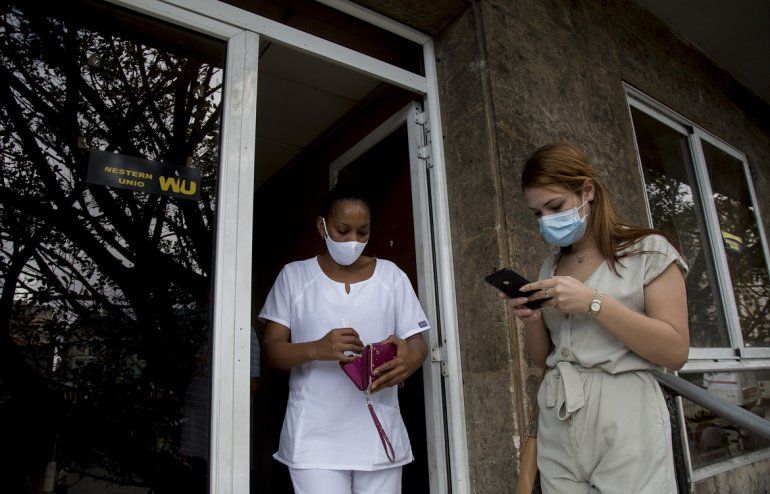 Una trabajadora de salud cubana deja una oficina de Western Union después de cobrar dinero mientras otra clienta espera su turno el último día de trabajo de la oficina en La Habana, Cuba, el lunes 23 de noviembre de 2020. 