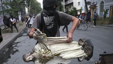 Un manifestante enmascarado remueve una estatua de Jesucristo de una iglesia para usarla en una barricada en Santiago de Chile el viernes 8 de noviembre de 2019.