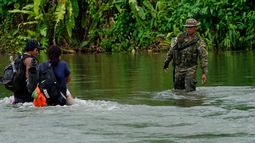 Un agente fronterizo panameño observa mientras dos migrantes cruzan el río Tuquesa tras recorrer a pie el Tapón del Darién, en Bajo Chiquito, Panamá, el 4 de octubre de 2023.&nbsp;