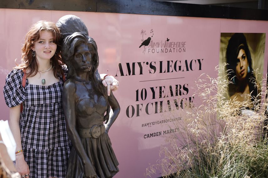 Un fan posa para una fotografía junto a una estatua de la cantante británica Amy Winehouse, instalada en el mercado de Camden en el norte de Londres, el 23 de julio de 2021, el décimo aniversario de su muerte.