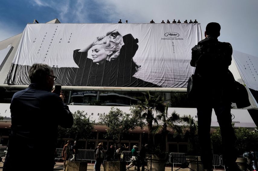 La gente observa cómo los trabajadores cuelgan el cartel oficial del 76º Festival de Cine de Cannes con una fotografía de la actriz Catherine Deneuve de Jack Garofalo, en la fachada del Palais des Festivals en Cannes, sureste de Francia, el 14 de mayo de 2023.
